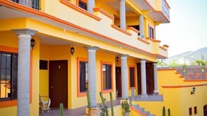 Un edificio de varios pisos con fachada amarilla y detalles en naranja, con balcones y un patio central con cactus.