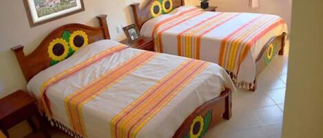 Habitación con dos camas, cada una adornada con una cabeza de girasol, un cuadro en la pared y una mesita de noche junto a una de las camas.