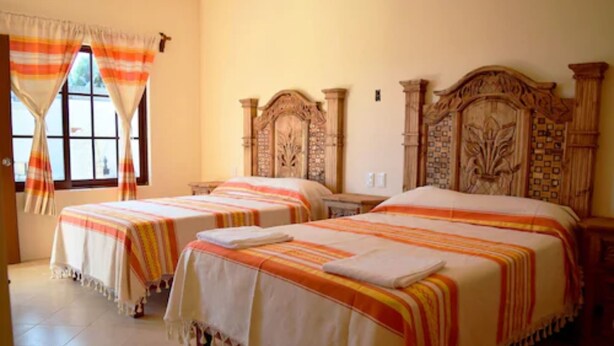 Habitación de hotel con dos camas, cada una con cabecero de madera, colcha a rayas y una ventana con cortinas.