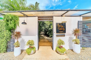 Entrada de hotel com caminho coberto, plantas em vasos e uma placa com a inscrição 'La Toca La Gata'.