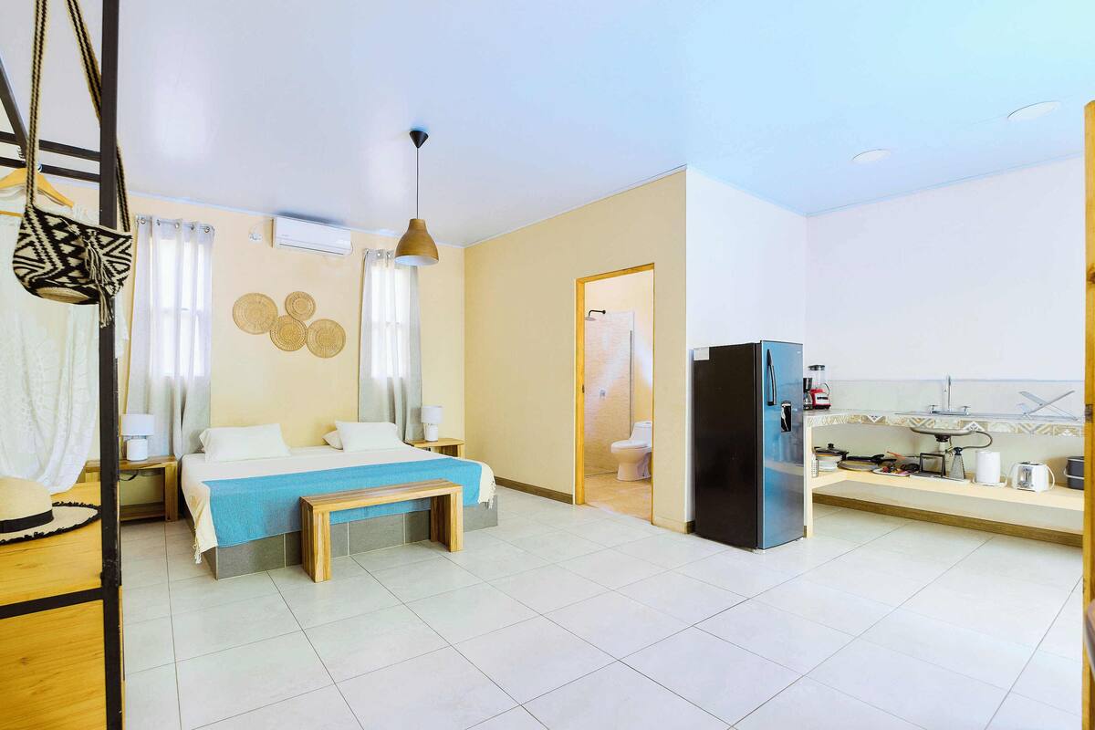 Habitación de hotel con cama, mesita de noche, sillón colgante y una zona de kitchenette.