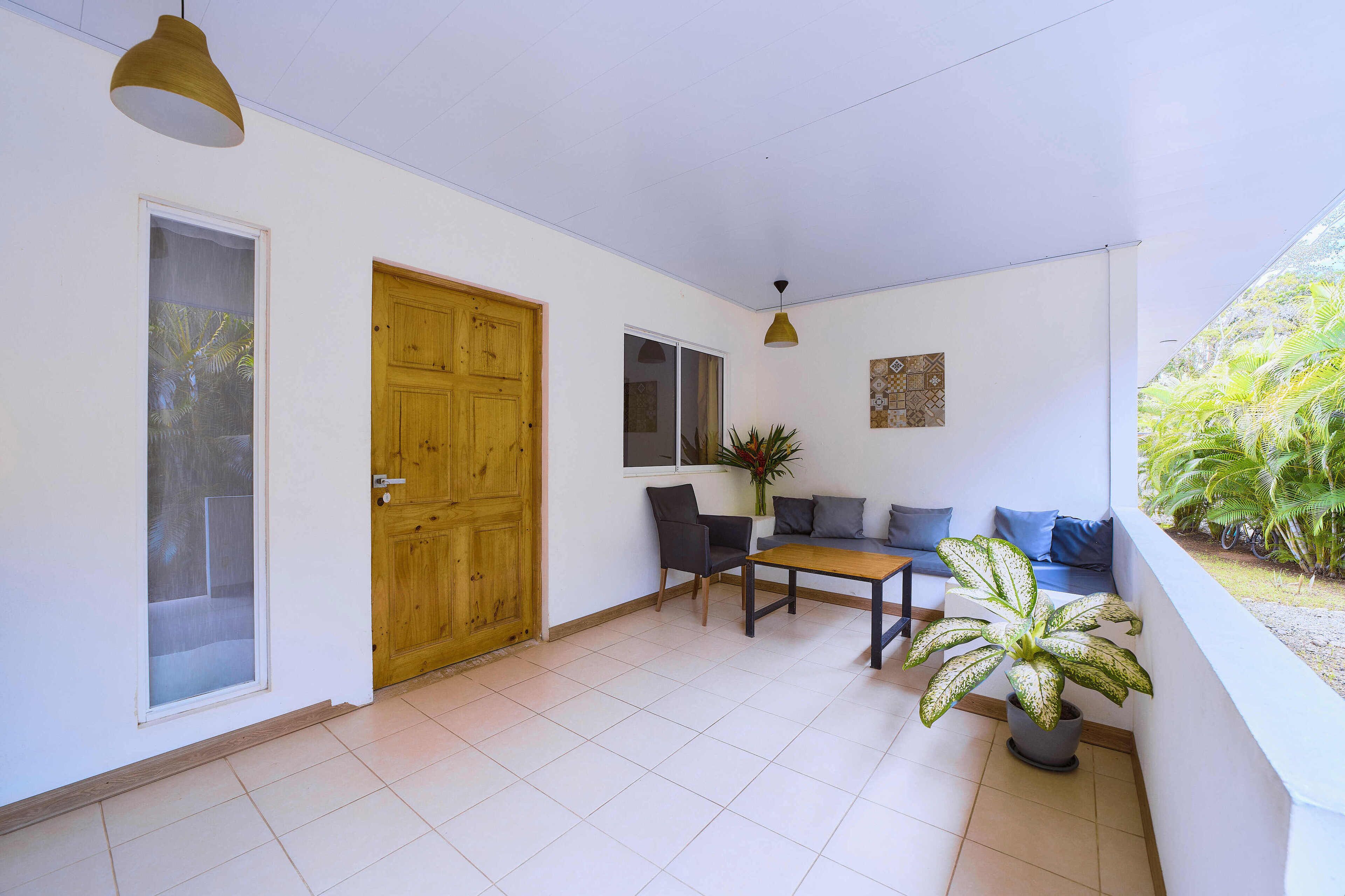 A room with a wooden door, a window, a table with chairs, a sofa, and a potted plant.
