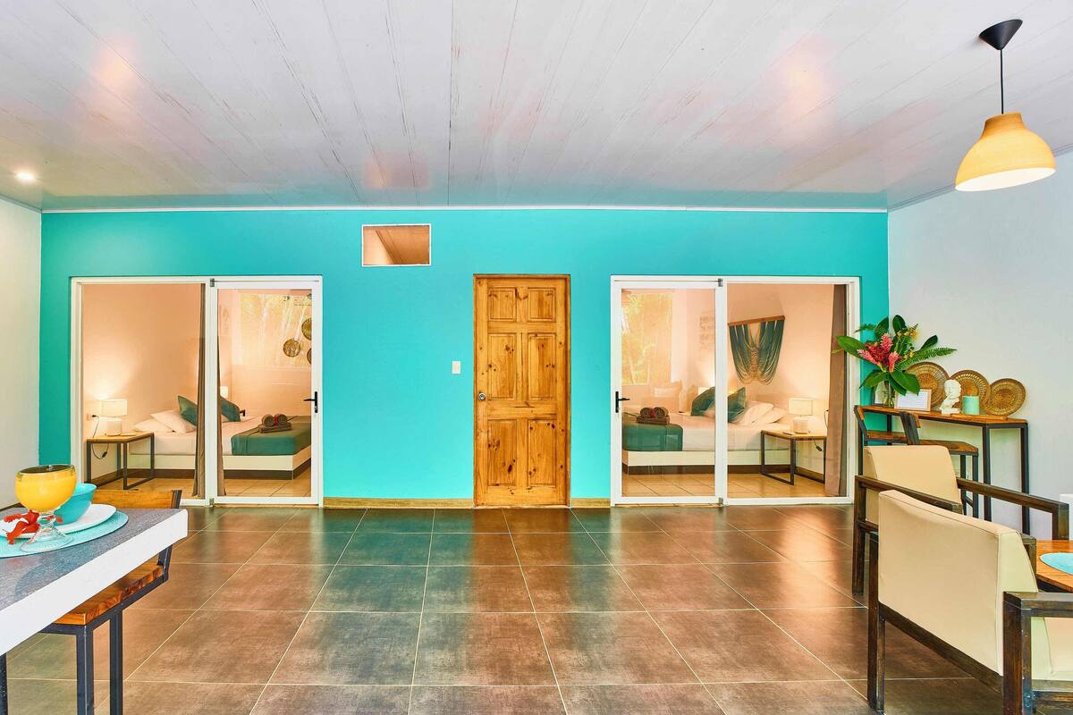 Una habitación amplia con una pared color turquesa, una puerta de madera y un comedor con mesa y sillas.