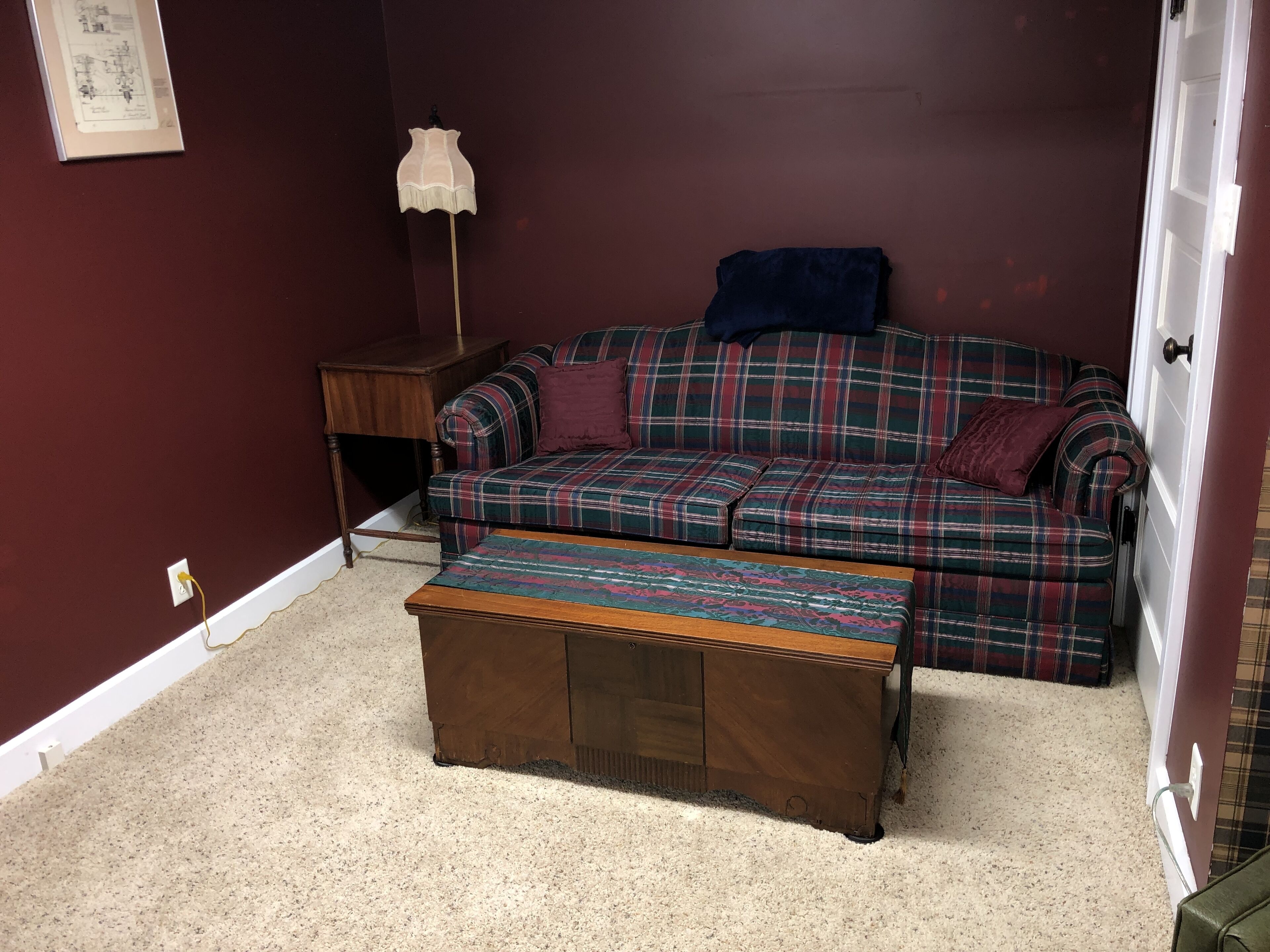 A living room with a plaid sofa, a matching ottoman, a small wooden side table, and a floor lamp.