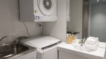 Een moderne badkamer met een ingebouwde wasmachine en droger, een roestvrijstalen wastafel en een spiegel boven het aanrecht.