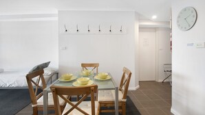 Una habitación de hotel compacta con zona de comedor que presenta una mesa dispuesta con cuencos y vasos amarillos, sillas de madera y un reloj de pared blanco.
