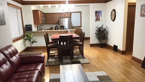 A living room with a leather sofa, a wooden coffee table, and a dining area with a red tablecloth. - Marvelous! Professionally Cleaned, Self Check In - Sleeps 14 (Racine)