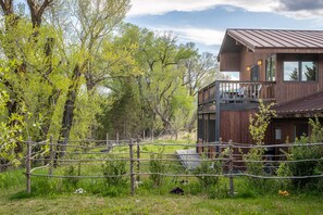 Situated in a lush landscape, this cabin features large windows and a wooden deck for outdoor relaxation.