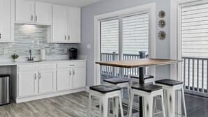Une cuisine avec des meubles blancs, une table en bois et des tabourets de bar.