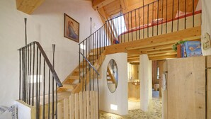 Una escalera de madera con barandilla, un espejo redondo y un suelo de piedra.