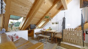 Una habitación acogedora en el ático con techo de madera, una pequeña mesa de comedor, bancos y un sofá.