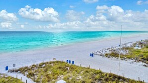 Une plage avec une eau turquoise et limpide, un rivage sablonneux et une zone herbeuse délimitée par une clôture.