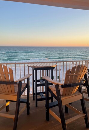 Ein Balkon mit Holzsesseln und einem Tisch, der auf den Sonnenuntergang über dem Meer blickt.