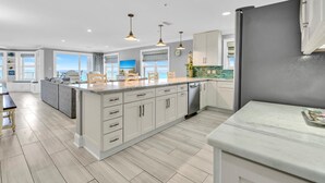 Une cuisine moderne avec des meubles blancs, un grand îlot central et des luminaires suspendus.