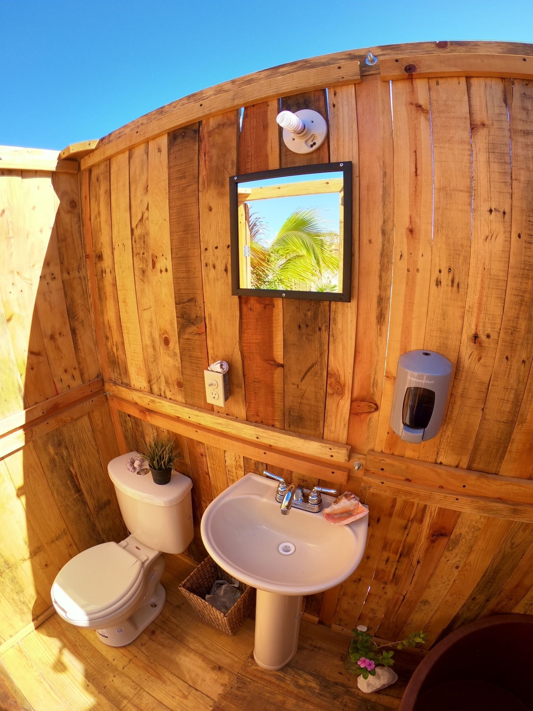 Eine Holzhütte mit Toilette, Waschbecken und einem an der Wand hängenden Bild von einer Palme.