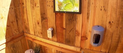 Eine Holzhütte mit Toilette, Waschbecken und einem an der Wand hängenden Bild von einer Palme.
