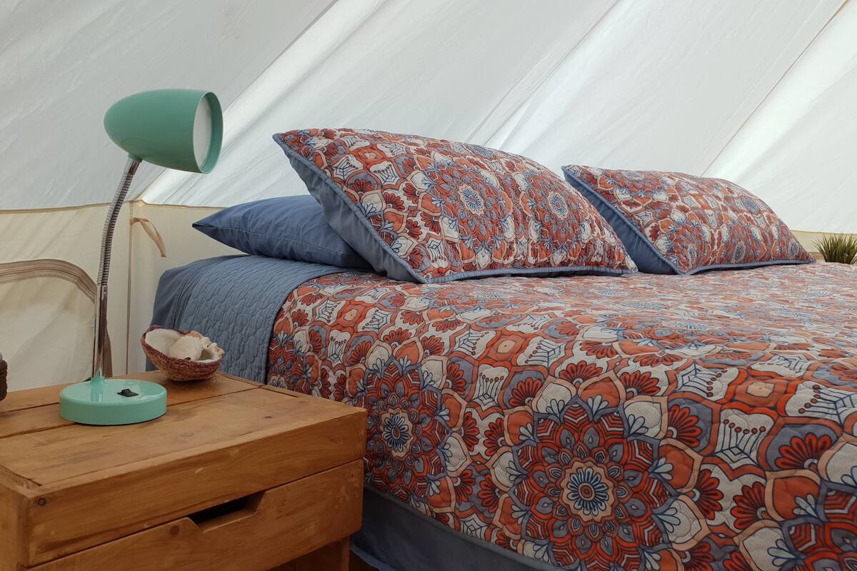 A tent with a bed, a wooden nightstand with a lamp, and a decorative bowl.