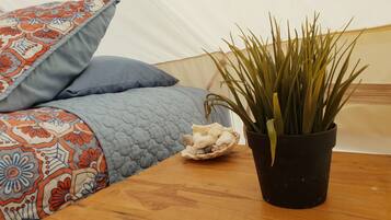 Una cama con un edredón y almohadas estampadas, una planta en maceta sobre una mesa de madera y un adorno pequeño.