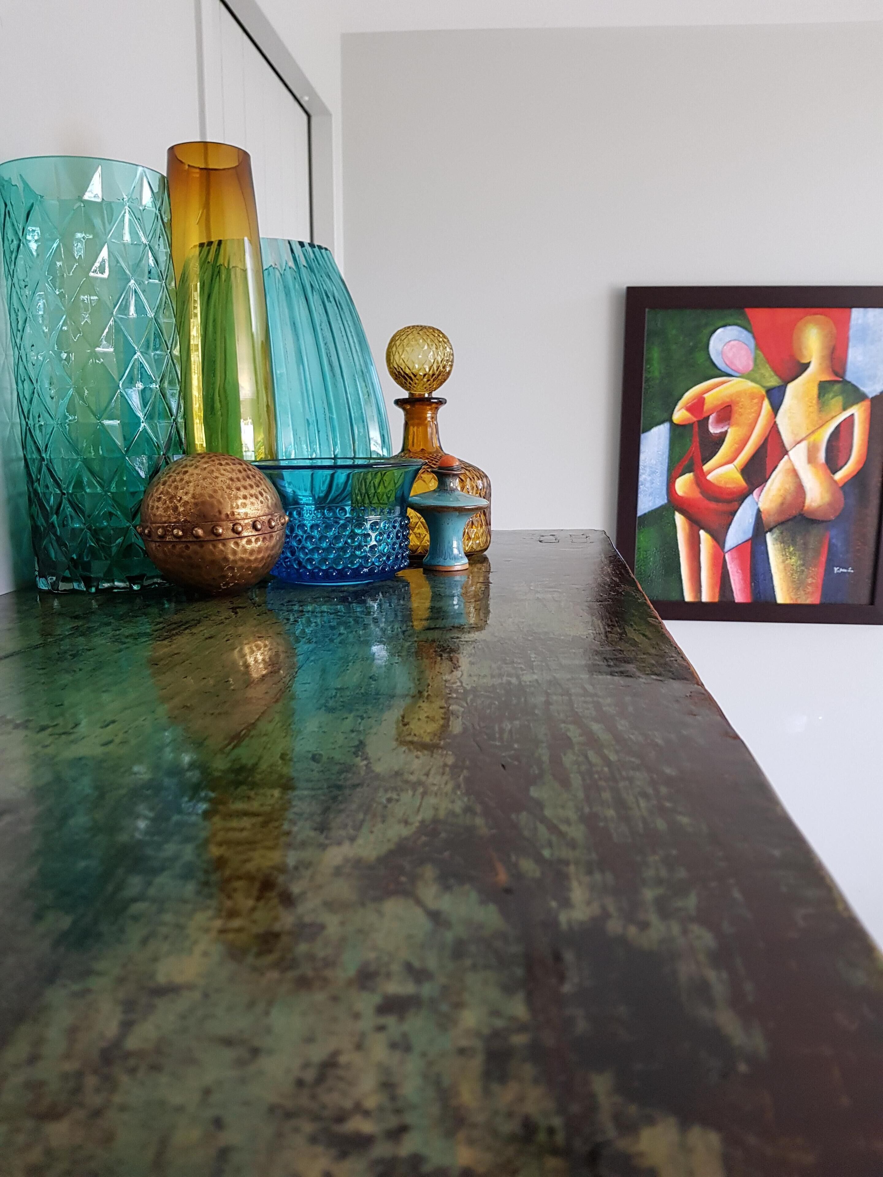 A variety of glass vases and a framed abstract painting on a reflective surface.