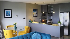 A modern living room with a blue sofa, yellow chairs, and a kitchen area with a built-in island.