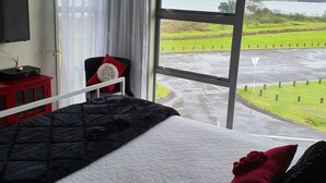 A bedroom with a large window, a bed, a TV, and a red cabinet.
