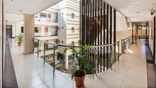 Un interior moderno con barandilla de vidrio, plantas en macetas y vista del exterior del edificio.