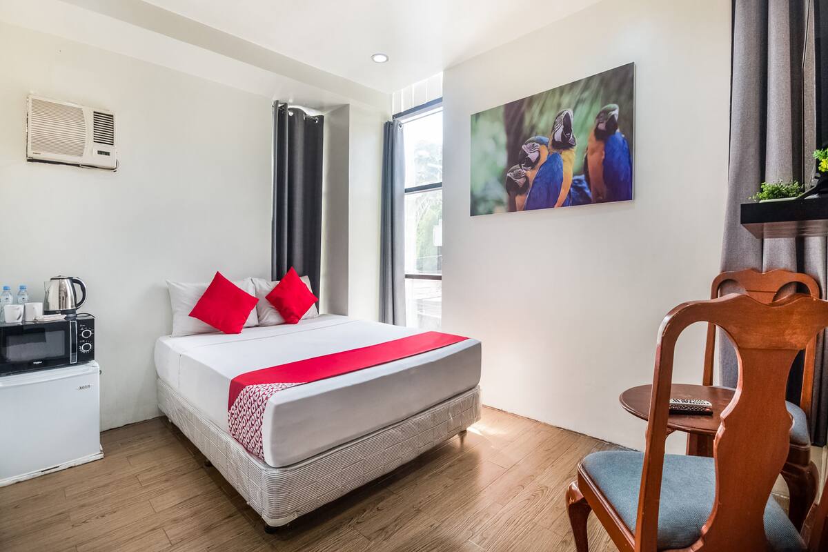 Une chambre d’hôtel avec un lit, une petite kitchenette, une chaise en bois et un tableau au mur.