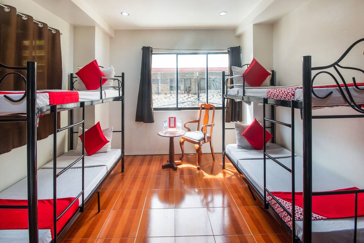 Une chambre de dortoir avec des lits superposés, une chaise en bois et une fenêtre donnant sur l’extérieur.