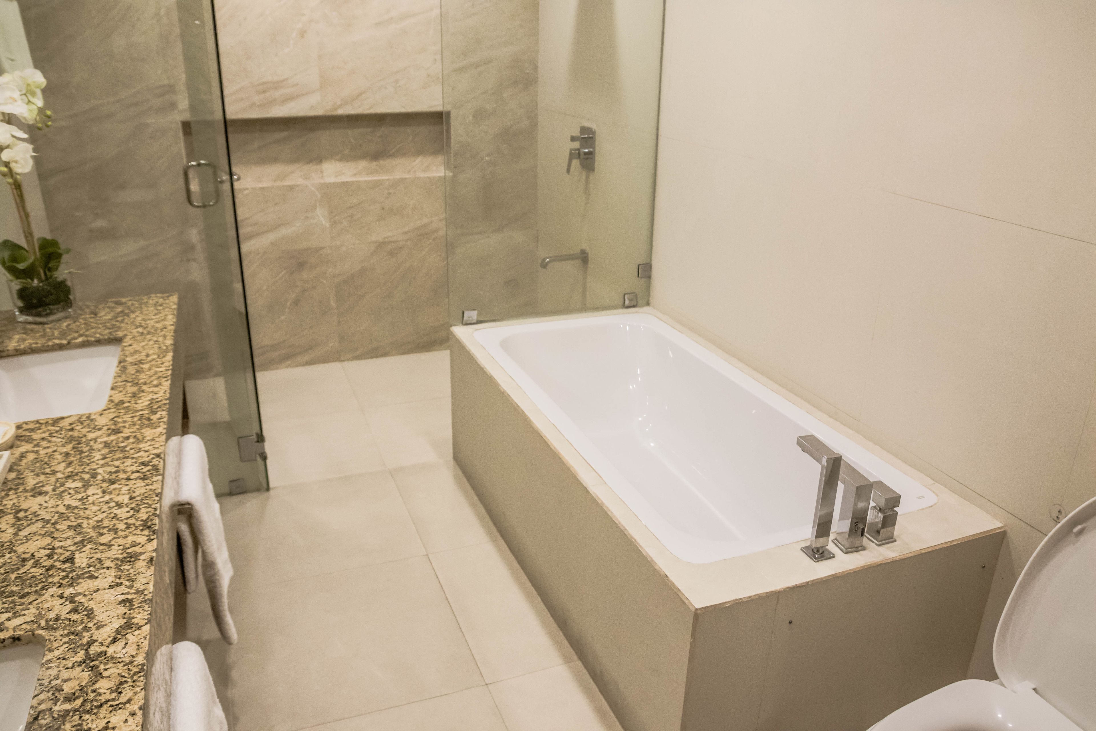 Un baño moderno con una bañera independiente, cabina de ducha con mampara de vidrio y encimera de granito con lavamanos y toallero.