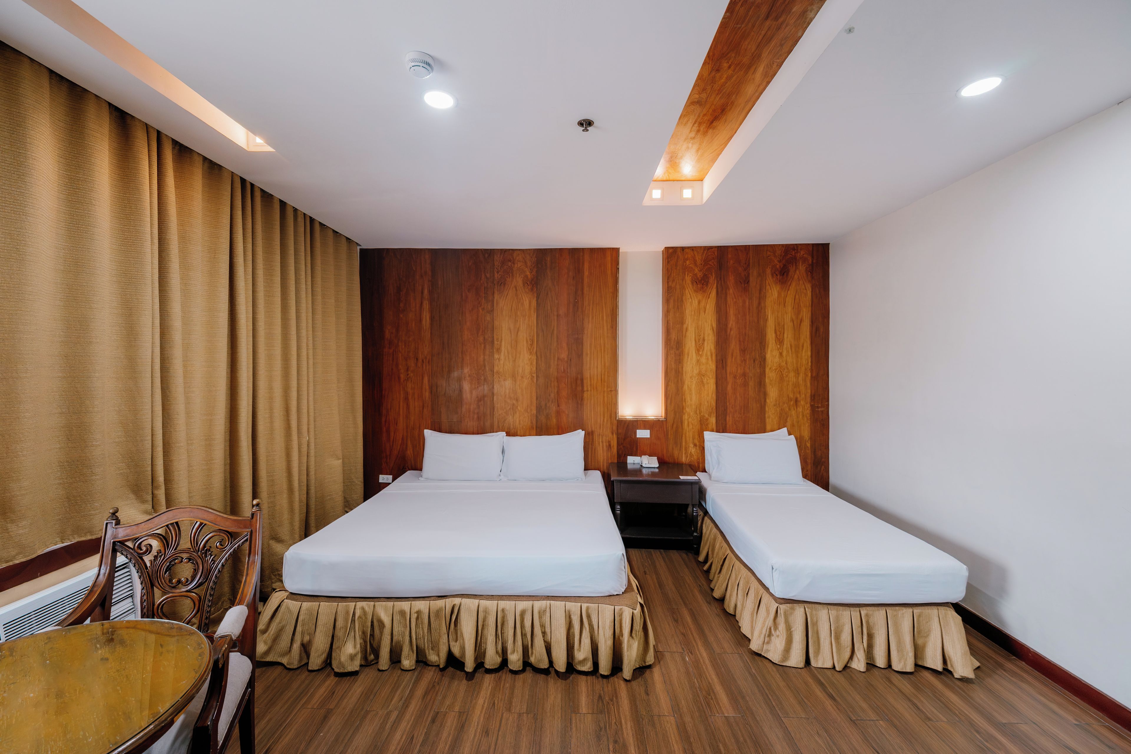A hotel room with two beds, a wooden headboard, a wooden floor, a table, and a chair.
