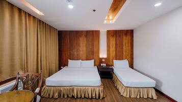 A hotel room with two beds, a wooden headboard, a wooden floor, a table, and a chair.