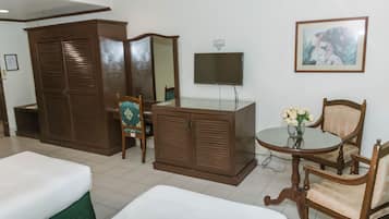 A hotel room with two beds, a wardrobe, a television, a small table with a vase of flowers, and a framed picture on the wall.