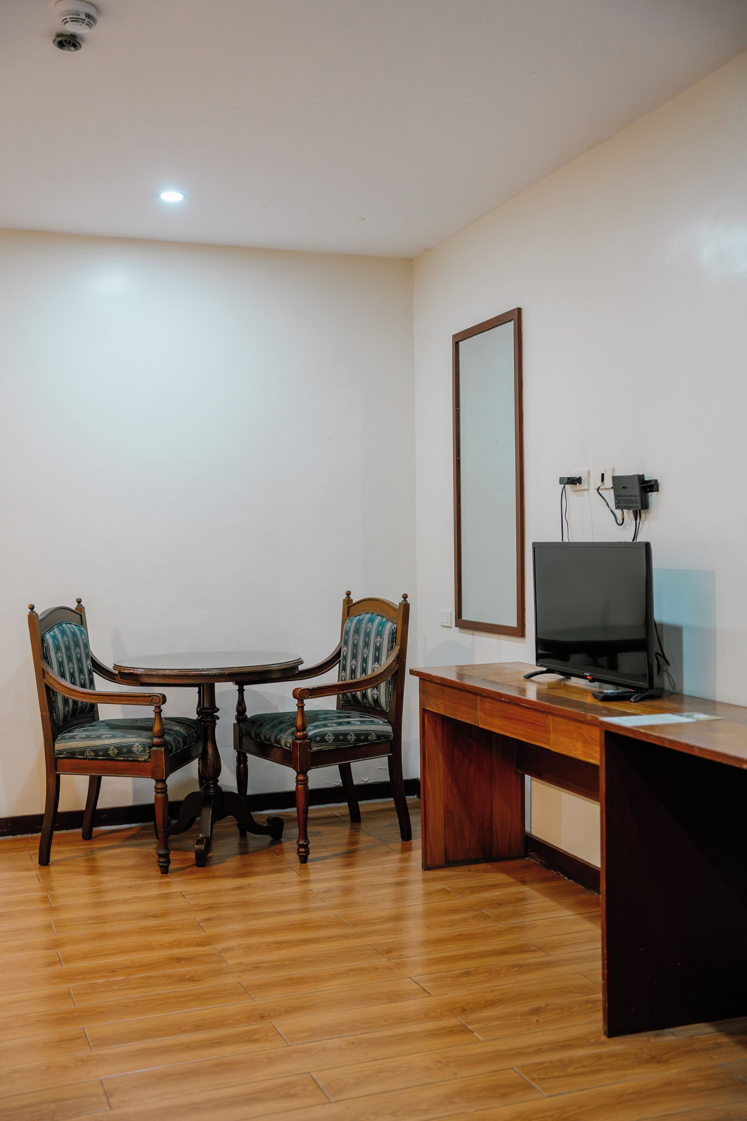 Une pièce avec un bureau en bois, deux chaises, un téléviseur et un miroir au mur.