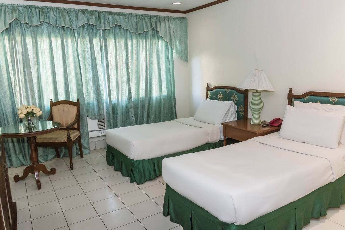 A hotel room with two beds, a desk with a chair, a lamp, and a vase of flowers.