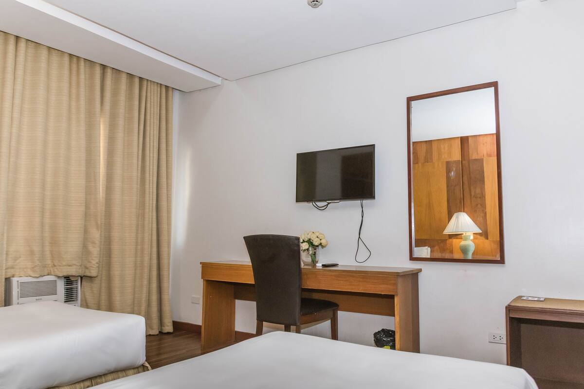 A hotel room with two beds, a desk with a chair, a television, a lamp, and a mirror.
