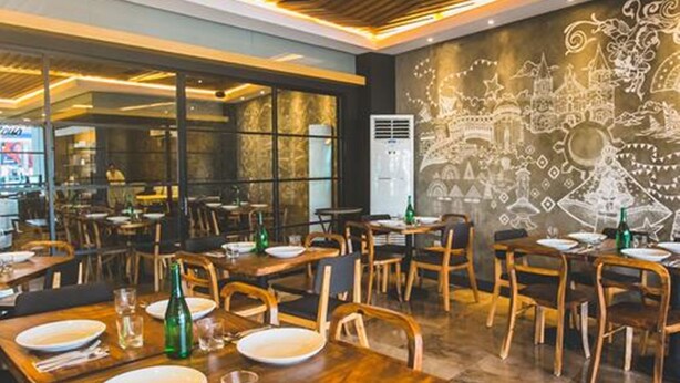 A restaurant with wooden tables and chairs, a mural on the wall, and a modern ceiling design. - La Fiesta Hotel (Iloilo)