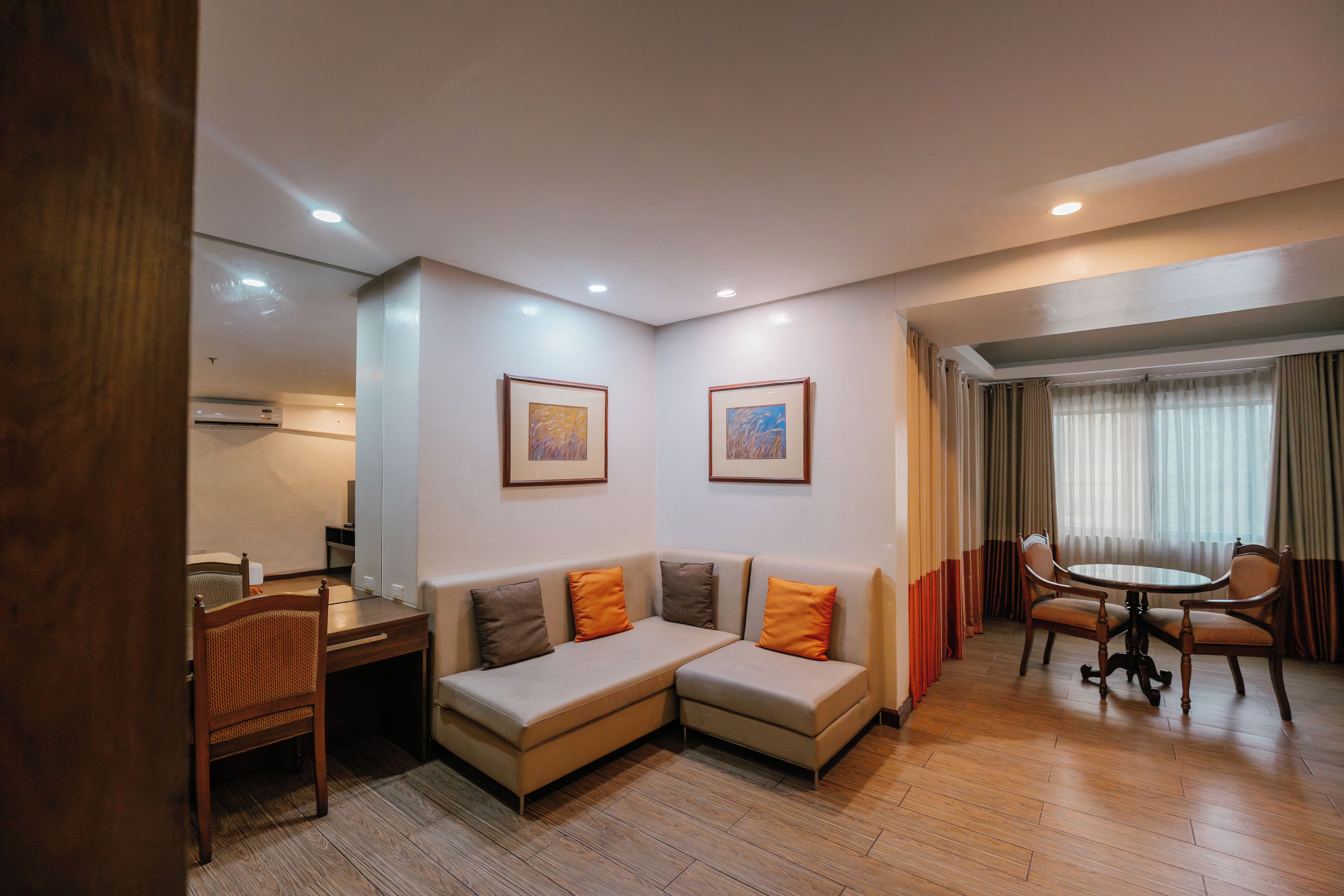 Una habitación de hotel con un sofá, una mesa de comedor y dos cuadros en la pared.