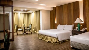 A hotel room with two beds, a dining area with a table and chairs, and a mirror. - La Fiesta Hotel (Iloilo)