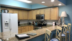 Una cocina con armarios de madera, un refrigerador, un microondas, una estufa y un dispensador de agua. Hay dos taburetes de bar con cojines estampados.