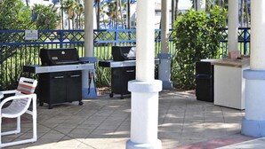 Un espacio al aire libre con dos parrillas, una silla blanca y un contenedor de basura.