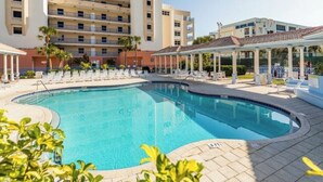 Una piscina con sillas de descanso y una zona de estar cubierta, rodeada por un edificio con varios balcones.