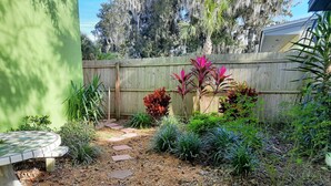A garden with a wooden fence, a stone pathway, and various plants.