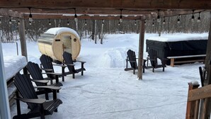 Un espacio al aire libre cubierto de nieve con sillas Adirondack y un barril de madera.