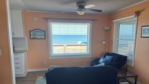 A bedroom with a bed, a ceiling fan, a window with blinds, a nightstand, and a view of the beach. - HipNautical Oceanfront (Kitty Hawk)