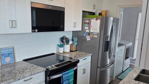A modern kitchen with white cabinets, stainless steel appliances, and a granite countertop. - HipNautical Oceanfront (Kitty Hawk)