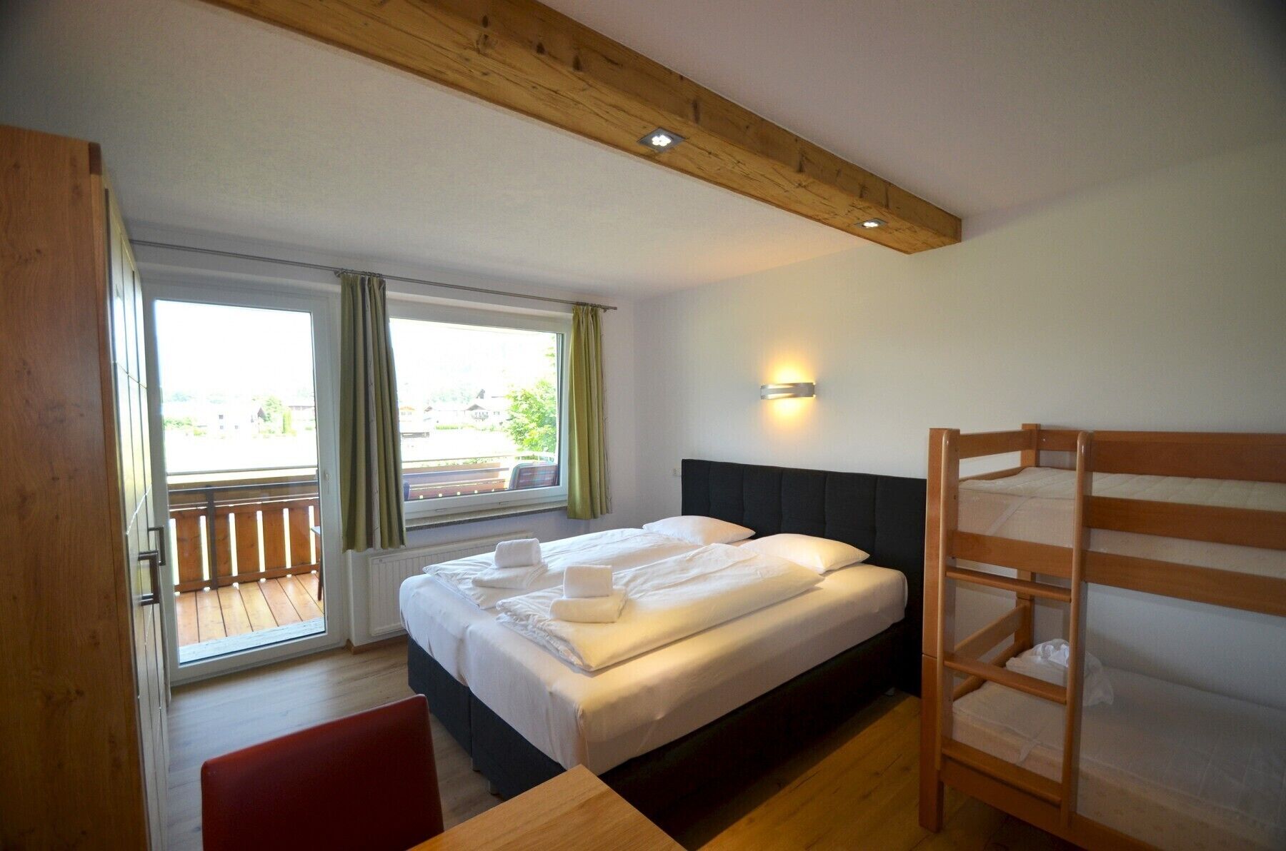 Ein Schlafzimmer mit einem Bett, einem Holzbett mit Etagen und einem Fenster mit Vorhängen sowie einer wandmontierten Leuchte.