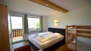 Une chambre à coucher avec un lit, un lit superposé en bois, une fenêtre avec des rideaux et un luminaire fixé au mur.
