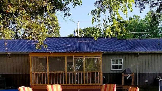 A rustic cabin with a metal roof, large windows, and a porch with striped chairs. - Lake front with dock and Beautiful view  (Afton)