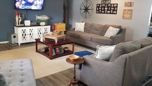 A living room with a grey sofa, a wooden coffee table, a white cabinet, and a TV mounted on the wall. - Lake front with dock and Beautiful view  (Afton)