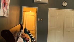 Een slaapkamer met een bed, een wandairconditioner, een klok en een deur die naar een andere kamer leidt.